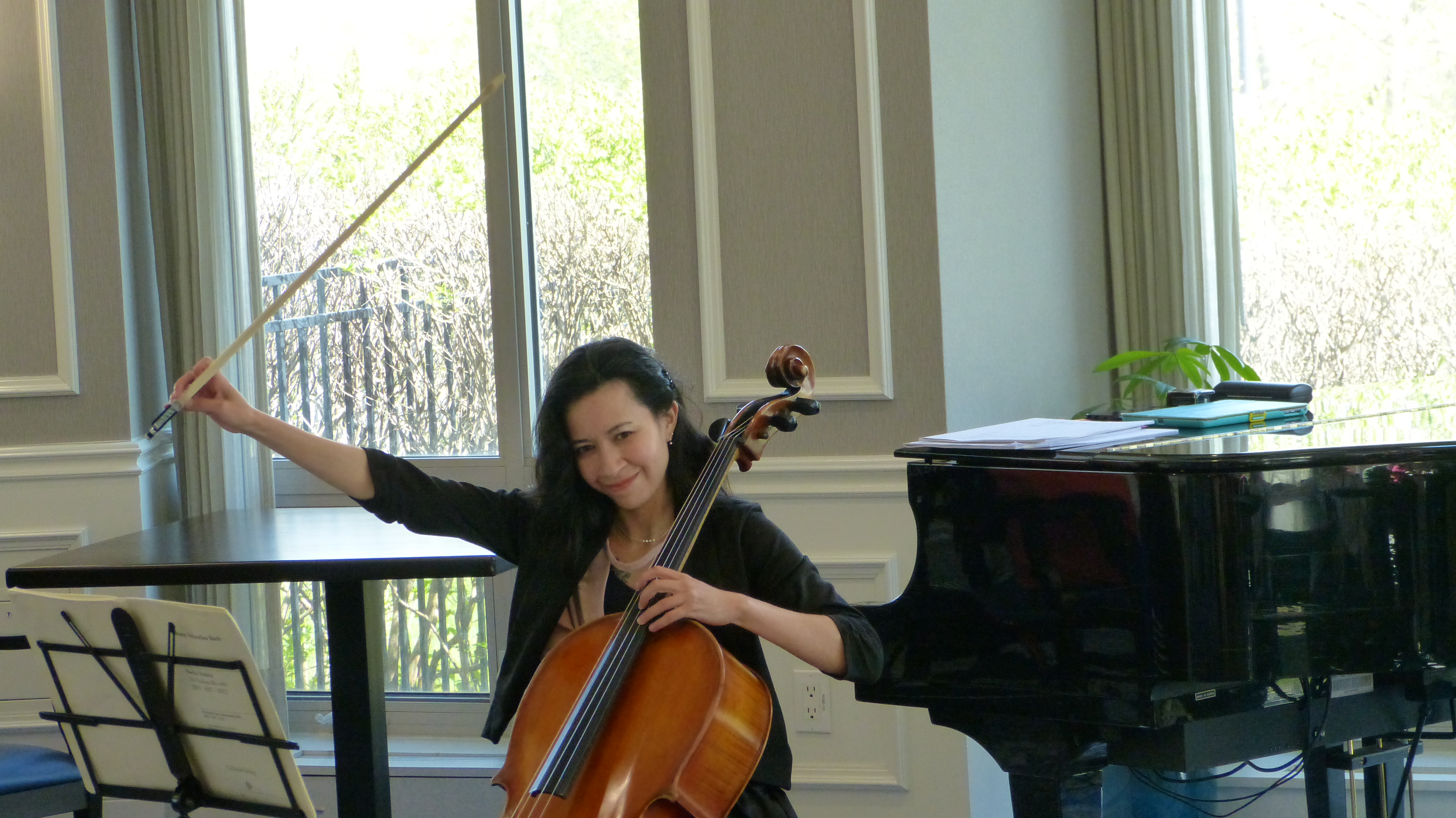 Cellist smiling mid-performance beside a grand piano