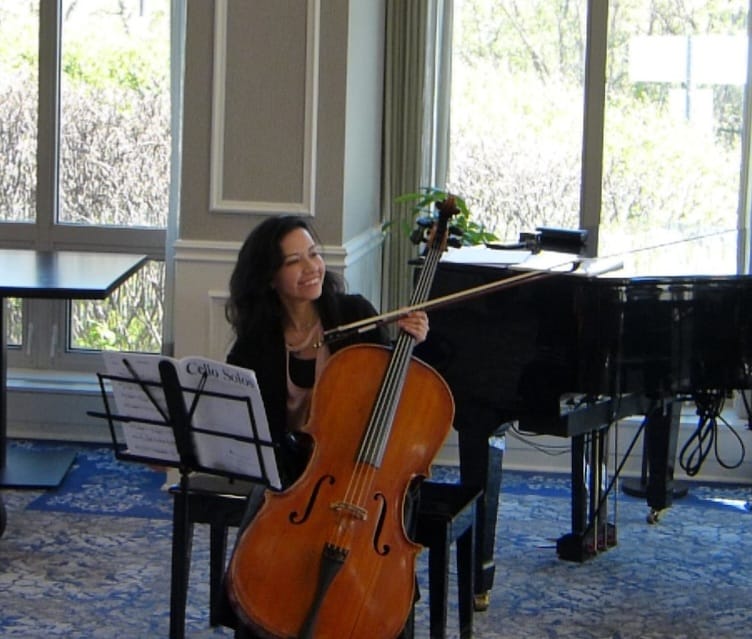 Karol Contreras smiling while playing cello beside a grand piano